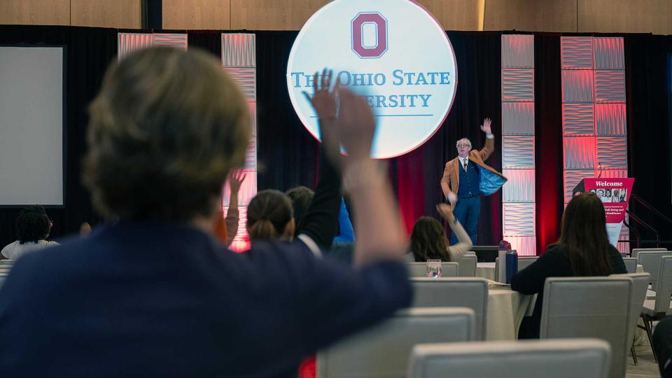 Audience members raise their hands while the speaker presents on stage